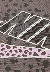 Audiniai su tekstūra, turintys rudą foną ir juodus gyvūnų raštus. Didelis, balta kontūra išsiskiriantis 'M', įspaustas dryžuotu zebriniu raštu ir rožiniu gepardo rašto akcentu.