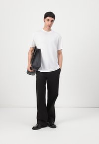 Zwarte tas, wit T-shirt met korte mouwen, losse zwarte broek en zwarte schoenen. Glad textuur en minimalistisch ontwerp, staand tegen een eenvoudige achtergrond.