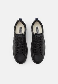 Svarta sneakers med ett texturerat mönster på sidorna, slät lädertå och runda snören. Har logotyp och en blå accent på hälen.