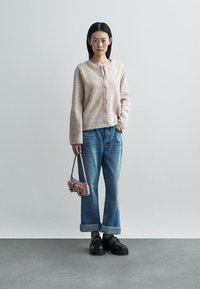 Beige knitted cardigan with round neckline and buttons, paired with blue wide-leg denim jeans, and a small pink handbag. Black platform shoes.