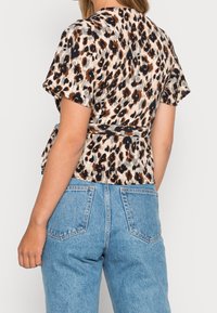 Femme portant un haut à manches courtes en imprimé léopard avec un lien à la taille et un jean en denim bleu clair taille haute, vue de dos.