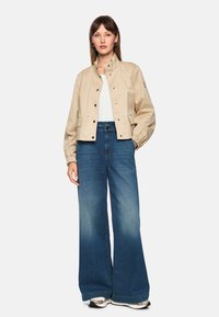 Beige cropped jacket made of lightweight fabric, featuring snap buttons, side pockets, and elastic cuffs. Paired with wide-leg faded blue jeans.