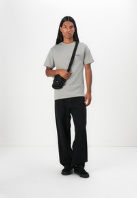 Grey cotton t-shirt with short sleeves and a purple graphic design, paired with black wide-leg pants and a small black crossbody bag.