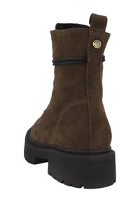 Bota corta de ante marrón con forma cilíndrica, suela de goma negra, cordón decorativo azul y un detalle dorado de marca en el talón.