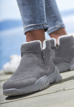 Gray ankle boots made of soft suede with white faux fur lining, side zip closure, and textured rubber sole. Casual design and sturdy shape.