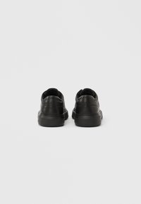 Ζευγάρι μαύρα δερμάτινα αθλητικά παπούτσια εμφανιζόμενα από πίσω σε ένα απλό ανοιχτό γκρι φόντο.