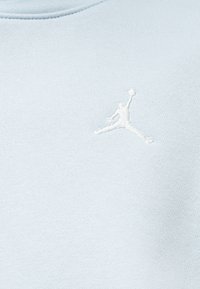 Λευκή κεντημένη σιλουέτα παίκτη μπάσκετ που πηδάει με μια μπάλα σε ανοιχτό μπλε ύφασμα, κοντά στη ραφή του γιακά.