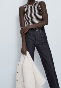 Black and white striped tank top, high-waisted dark denim jeans, and a white textured coat held in hand. Black belt with silver buckle.