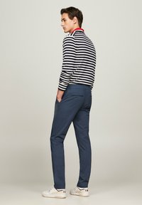 Camicia a maniche lunghe a righe con righe orizzontali blu navy e bianche; colletto rosso. Pantaloni slim-fit blu navy con tasca sul retro, abbinati a sneakers bianche.