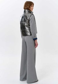 Metallisch graue, gepolsterte Weste mit hohem Kragen, kombiniert mit hellgrauen, weit geschnittenen Hosen. Der Stoff hat eine glatte Textur. Einfaches Design, minimale Akzente.