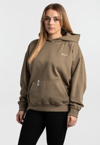 Olivgrön hoodie med en framficka, ribbade muddar och fåll. Har en liten logotyp på bröstet och en liten etikett på fickan.
