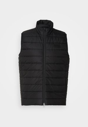 Vesta puffer neagră cu guler înalt, fermoar frontal, model de cusături orizontale și branding minim pe pieptul stâng.