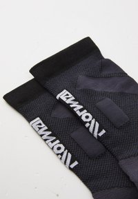 Mangas deportivas negras con patrones texturizados, que presentan un puño grueso y una marca blanca. El material parece transpirable y elástico.