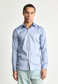 Svijetloplena košulja dugih rukava, napravljena od glatkog materijala, s kopčanjem na dugmad i kontrastnim manžetama. Slim fit dizajn s suptilnom teksturom.