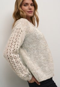 Cream-colored knit sweater with a loose fit, featuring textured, openwork sleeves and a solid body. Soft, fluffy yarn with ribbed cuffs.