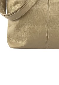 Beige leren schoudertas met een gestructureerde afwerking, met een zachte vorm, een enkele schouderriem en zichtbare stiksels.