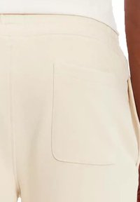 Beige broek met een rechthoekige achterzak, een gladde textuur en netjes gestikte naden. De tailleband is plat en eenvoudig.
