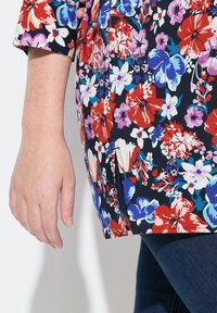 Bluse med blomsterprint på marineblå baggrund, prydet med røde, lilla og blå blomster, kortærmet og med en sideslidsdetalje.