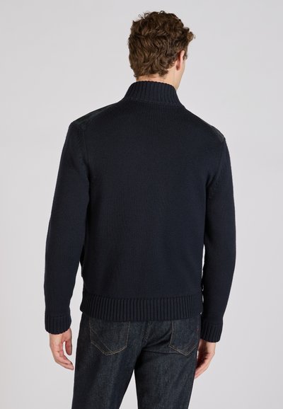 Granatowy sweter dziany z wysokim kołnierzem, ściągaczami na mankietach i pasku w talii. Z dodatkami ze skóry na ramionach i fakturowanym wykończeniem tkaniny.