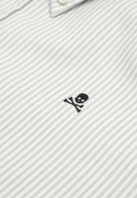 Gestreiftes Polohemd aus grauem und weißem Stoff mit einem schwarzen gestickten Totenkopf und gekreuzten Knochen über dem linken Brustbereich.