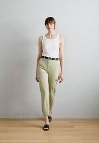 Top alb din bumbac, pantaloni cargo verzi deschis cu buzunare, curea neagră cu o cataramă circulară și sandale negre cu talpă joasă. Texturi netede în întreaga ținută.