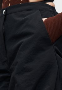 Μαύροι παντελόνες από ελαφρύ ύφασμα, με απαλή υφή, πλαϊνές τσέπες και κλείσιμο με φερμουάρ και κουμπί στη μέση.