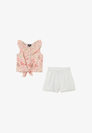 Haut sans manches à imprimé floral avec col à volants et devant à nouer ; associé à un short léger blanc avec une taille élastique.