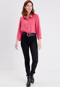 Chemisier rose à pois blancs, manches longues retroussées aux poignets, associé à un jean skinny noir et des bottines noires.