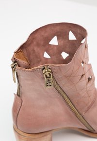 Bottine en cuir rose avec fermeture éclair latérale, motifs triangulaires découpés près du haut, et talon en bois empilé.