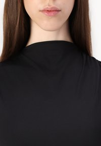 Fekete, magas nyakú ruha sima textúrával, testhezálló fazonnal és minimalista stílussal. Kiemelkedően figyel a nyakkivágás formájára és a szövet esésére.