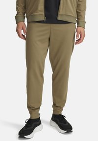 Oliven grønne joggerbukser med slim fit, elastiske bukseafslutninger, sidelommer og en glat tekstur. Båret med sorte sportsko.
