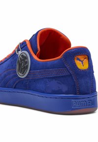 Niebieskie zamszowe sneakersy z pomarańczowymi akcentami, zaokrąglony czubek, teksturowana powierzchnia oraz okrągła metka z logo. Markowe logo PUMA na pięcie i boku.