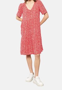 Robe fleurie rouge à manches courtes, décolleté en V et design à volants. Fabriquée en tissu léger, assortie à des baskets blanches.