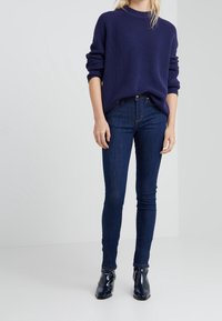 Pull en maille côtelée bleu marine avec un col rond, associé à un jean foncé ajusté et des bottines noires brillantes. Design simple et épuré.