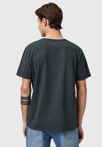 Dunkelgraues kurzärmliges T-Shirt mit Rundhalsausschnitt und lockerer Passform. Der Stoff wirkt weich mit einer glatten Textur; kombiniert mit hellblauen Jeans.
