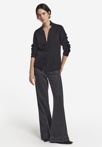 Svart stickad cardigan med ståkrage, knäppning, ribbade muddar och två framfickor, tillsammans med mörka vida jeans.