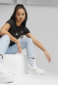 T-shirt nera con logo stampato, jeans azzurri chiari, sneakers bianche con platform e accenti pastello, calzini a righe, sfondo minimalista.