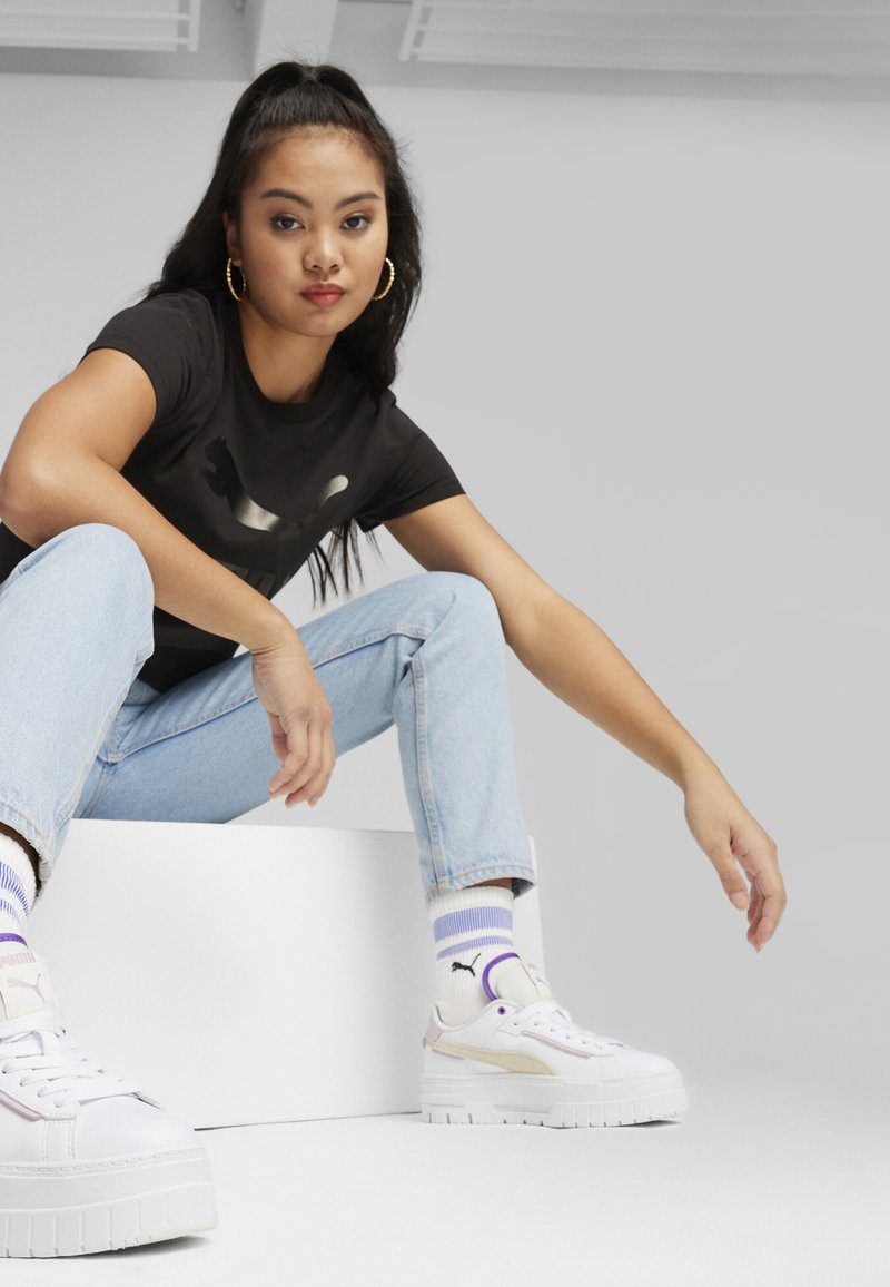 T-shirt nera con logo stampato, jeans azzurri chiari, sneakers bianche con platform e accenti pastello, calzini a righe, sfondo minimalista.