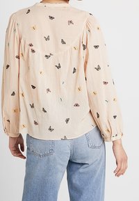 Blusa color pescoce con maniche lunghe a sbuffo, decorata con ricami di farfalle colorate. Tessuto morbido e testurizzato con orlo arrotondato e vestibilità morbida.
