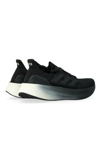 Un paio di scarpe da ginnastica nere basse con suole bianche a gradiente spesse e strisce nere su uno sfondo bianco.