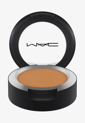 Okrągłe kompaktowe lusterko o czarnej obudowie i srebrnej obręczy, zawierające gładki, matowy proszek w średnim odcieniu brązu. Nazwa marki widoczna na pokrywce.