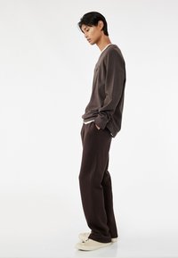 Brun sweatshirt med rund hals, grå accenter og matchende tapered bukser. Sneakers er cremefarvede. Enkel, afslappet pasform.