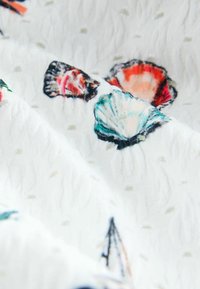 Țesătură din bumbac cu un fundal alb și modele colorate de scoici în nuanțe de albastru, portocaliu și roz, texturate cu mici puncte ridicate.