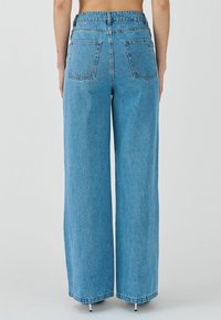 Jeans de tiro alto de mezclilla de corte ancho en azul claro. Presentan dos bolsillos traseros y un dobladillo sin rematar con un ligero desgaste.