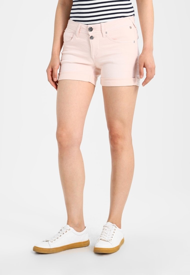 Shorts de mezclilla de color rosa claro con dobladillo enrollado, que presentan dos bolsillos delanteros, dos bolsillos traseros y un cierre con botón. Combinados con zapatillas blancas.