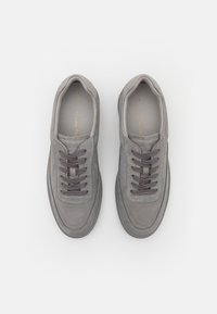 Gray suede sneakers with a rounded toe, flat lace-up design, and textured accents. Features dark gray laces and branding inside.