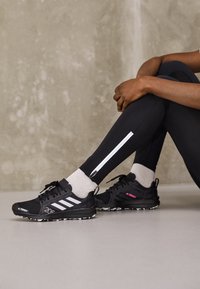 Scarpe da ginnastica nere con accenti bianchi, materiale testurizzato e suola con motivo, abbinate a leggins neri con un dettaglio zip bianco.