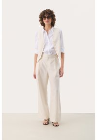 Gilet beige a righe e pantaloni a vita alta abbinati, indossati con una camicia bianca a maniche lunghe e sandali neri con tacco.