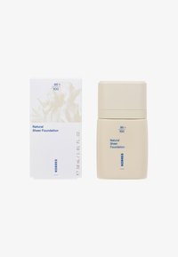Natural Sheer Foundation in a beige, cylindrical container with a twist cap. Accompanied by a white box featuring light floral design and blue text.