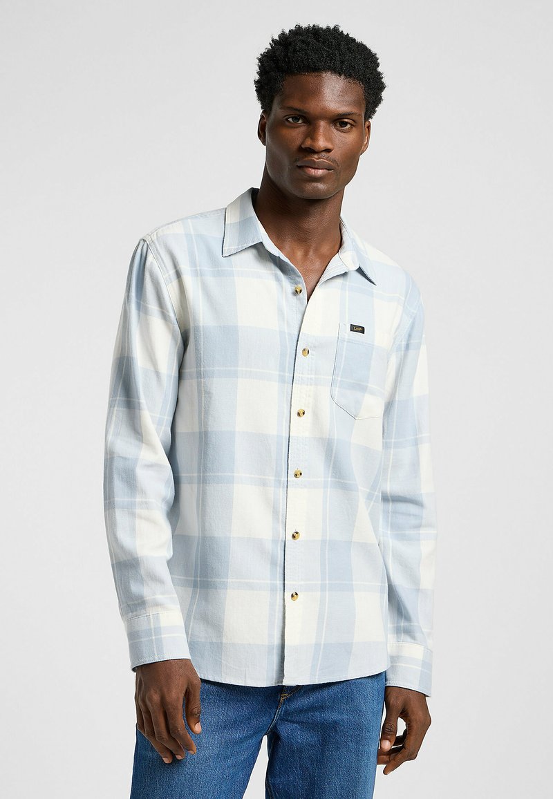 Camisa de manga larga a rayas en tonos azul claro y blanco, con cuello abotonado, bolsillo en el pecho y botones dorados, fabricada en una tela suave.